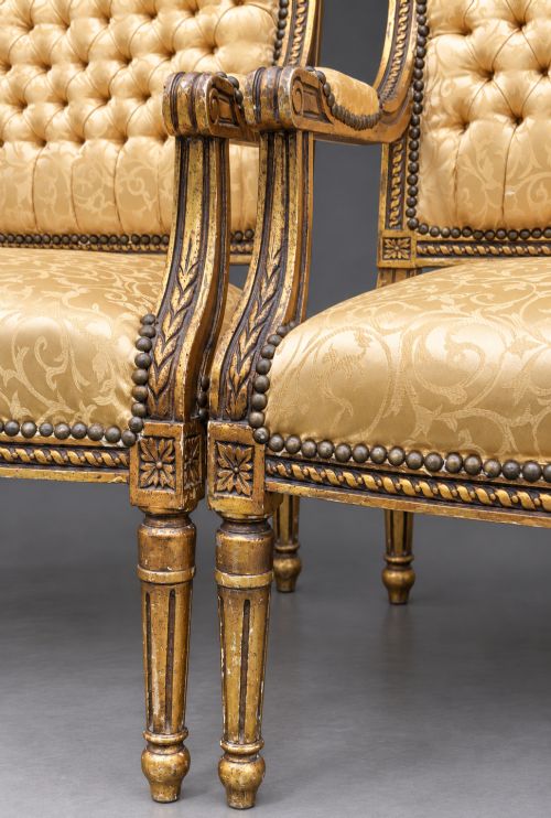 fig 7. A pair of 19th-century giltwood open armchairs featuring carved leaf detailing, button-tufted gold damask upholstery, and fluted front legs.