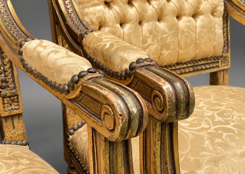 fig 9. A pair of 19th-century giltwood open armchairs featuring carved leaf detailing, button-tufted gold damask upholstery, and fluted front legs.