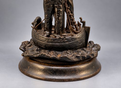 fig 3. A nineteenth-century dark patinated bronze sculpture depicting two fishermen standing in a small vessel atop sculpted ocean waves, mounted on a rounded base.