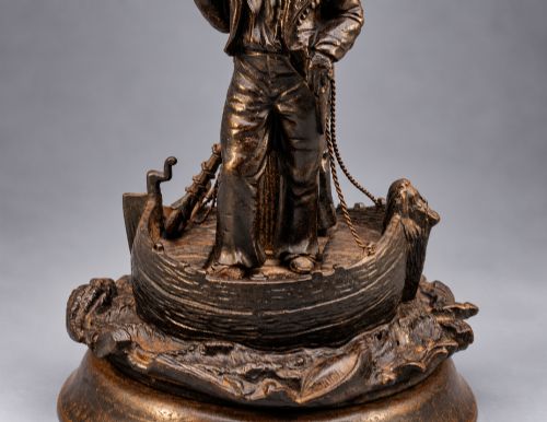fig 6. A nineteenth-century dark patinated bronze sculpture depicting two fishermen standing in a small vessel atop sculpted ocean waves, mounted on a rounded base.