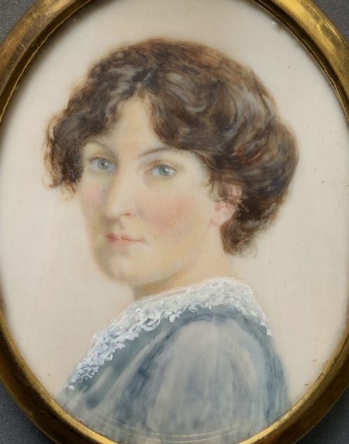 fig 1. An Edwardian oval watercolour portrait miniature depicting a lady with dark curly hair and a lace-collared blue dress, set within a gilt brass frame with a hanging ring.