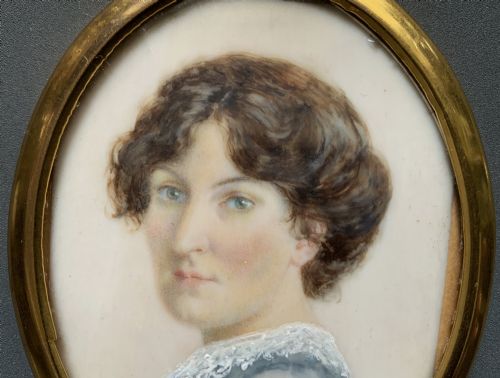fig 4. An Edwardian oval watercolour portrait miniature depicting a lady with dark curly hair and a lace-collared blue dress, set within a gilt brass frame with a hanging ring.