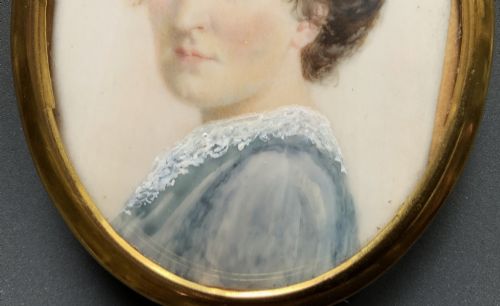 fig 5. An Edwardian oval watercolour portrait miniature depicting a lady with dark curly hair and a lace-collared blue dress, set within a gilt brass frame with a hanging ring.