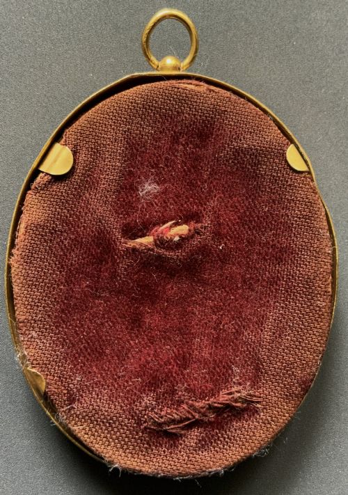 fig 6. An Edwardian oval watercolour portrait miniature depicting a lady with dark curly hair and a lace-collared blue dress, set within a gilt brass frame with a hanging ring.