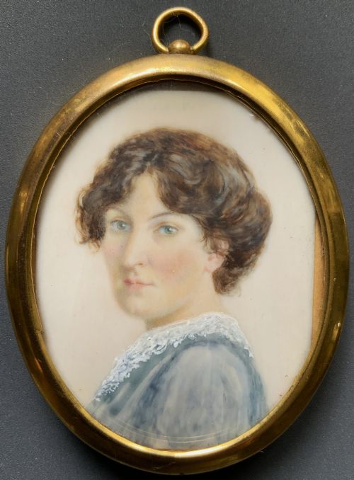 fig 7. An Edwardian oval watercolour portrait miniature depicting a lady with dark curly hair and a lace-collared blue dress, set within a gilt brass frame with a hanging ring.