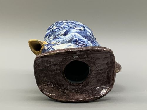 fig 8. An 18th-century Dutch Delftware ceramic jug hand-painted in blue, white, brown, and yellow, designed in the form of a seated monkey in a tricorn hat holding a cup.