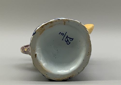 fig 9. An 18th-century Dutch Delftware ceramic jug hand-painted in blue, white, brown, and yellow, designed in the form of a seated monkey in a tricorn hat holding a cup.