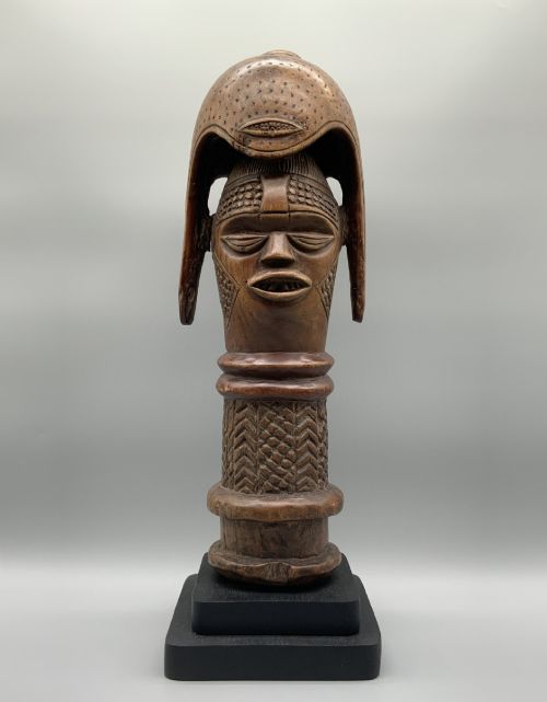 fig 1. A carved brown wooden African Mende Sowei staff finial depicting a stylised head with crest, mounted on a square black plinth.