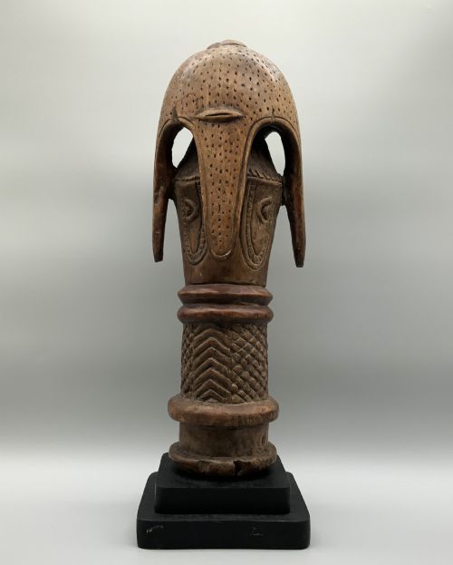 fig 3. A carved brown wooden African Mende Sowei staff finial depicting a stylised head with crest, mounted on a square black plinth.