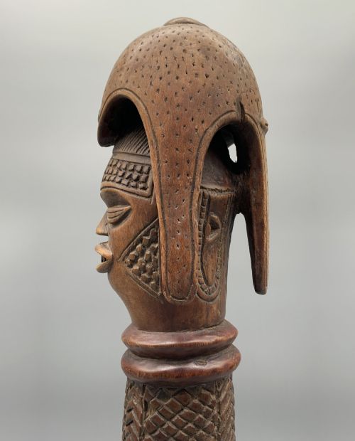 fig 5. A carved brown wooden African Mende Sowei staff finial depicting a stylised head with crest, mounted on a square black plinth.
