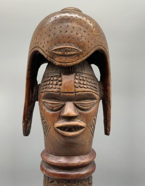 fig 8. A carved brown wooden African Mende Sowei staff finial depicting a stylised head with crest, mounted on a square black plinth.