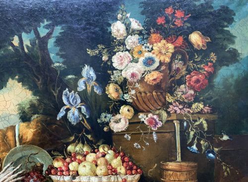fig 6. A classical oil painting displaying a bowl of fruit, a urn with flowers, asparagus, and melons set against a dark landscape backdrop within a carved silver-grey frame.