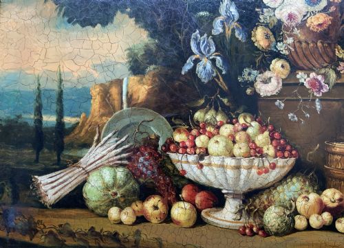 fig 8. A classical oil painting displaying a bowl of fruit, a urn with flowers, asparagus, and melons set against a dark landscape backdrop within a carved silver-grey frame.