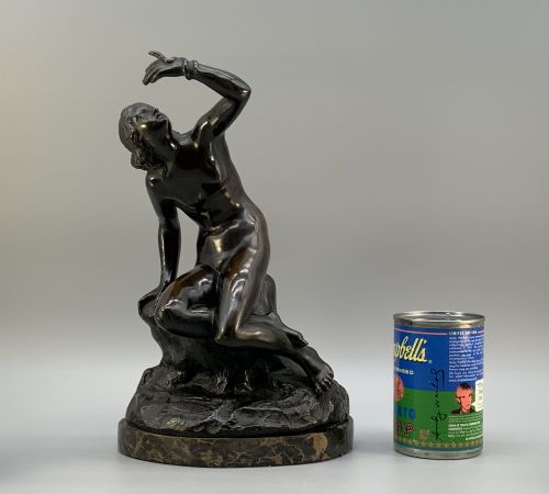 fig 1. A patinated dark bronze sculpture depicting a classical female figure reaching upward while seated on a rocky outcrop atop a circular marble base.