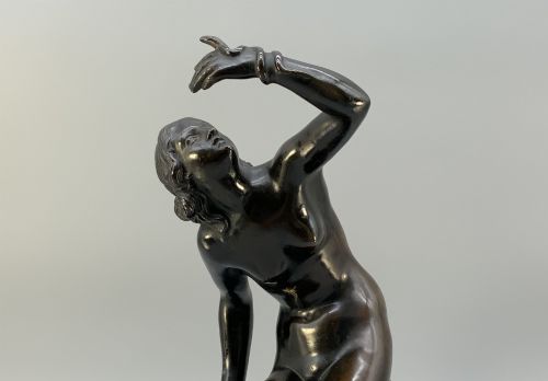 fig 2. A patinated dark bronze sculpture depicting a classical female figure reaching upward while seated on a rocky outcrop atop a circular marble base.