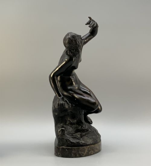 fig 4. A patinated dark bronze sculpture depicting a classical female figure reaching upward while seated on a rocky outcrop atop a circular marble base.