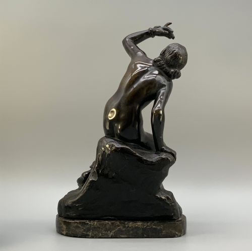 fig 5. A patinated dark bronze sculpture depicting a classical female figure reaching upward while seated on a rocky outcrop atop a circular marble base.
