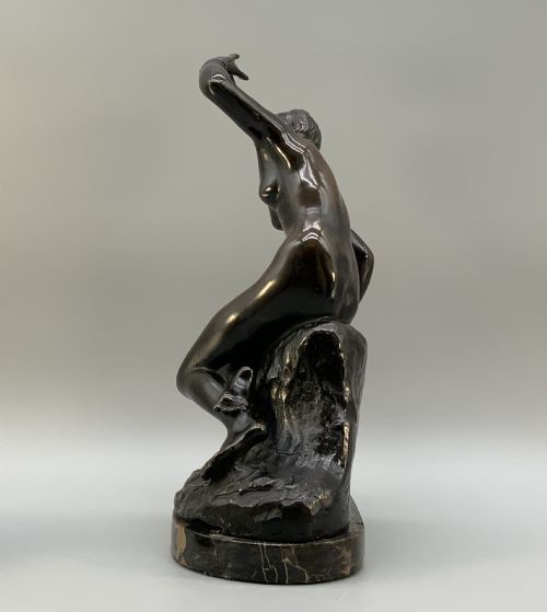 fig 6. A patinated dark bronze sculpture depicting a classical female figure reaching upward while seated on a rocky outcrop atop a circular marble base.
