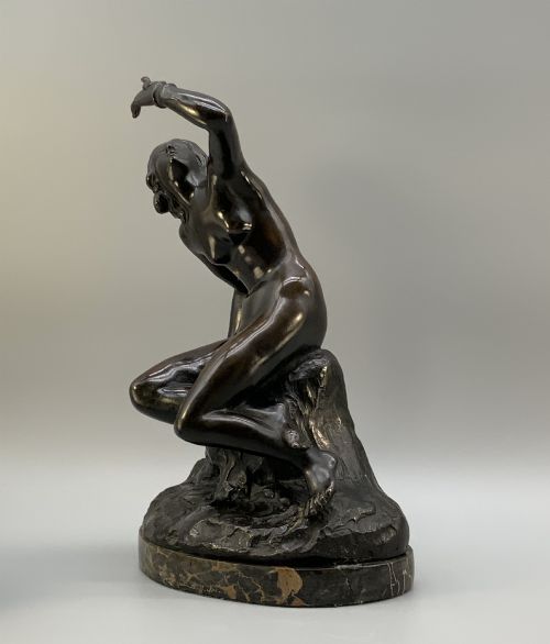 fig 7. A patinated dark bronze sculpture depicting a classical female figure reaching upward while seated on a rocky outcrop atop a circular marble base.