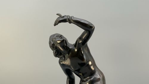 fig 8. A patinated dark bronze sculpture depicting a classical female figure reaching upward while seated on a rocky outcrop atop a circular marble base.
