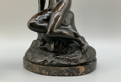 fig 10. A patinated dark bronze sculpture depicting a classical female figure reaching upward while seated on a rocky outcrop atop a circular marble base.