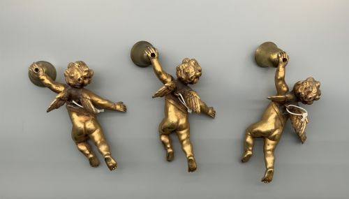 fig 1. A set of three gilt metal wall sconces crafted in the shape of winged cherubs holding bell-shaped light sockets.