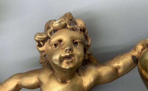 fig 3. A set of three gilt metal wall sconces crafted in the shape of winged cherubs holding bell-shaped light sockets.