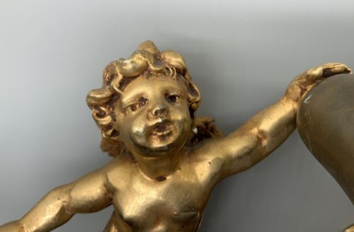 fig 4. A set of three gilt metal wall sconces crafted in the shape of winged cherubs holding bell-shaped light sockets.