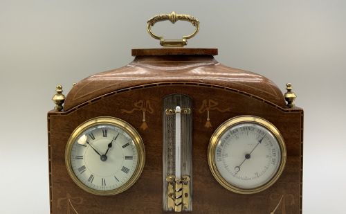 fig 4. An Edwardian mahogany desk compendium featuring an inlaid floral swag motif, central thermometer, clock dial, barometer dial, and top brass handle.