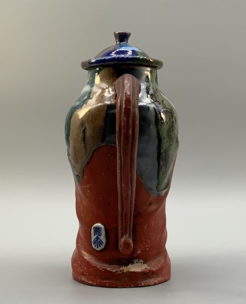 fig 3. An antique Japanese Sumida Gawa lidded pottery jug sculpted in the form of a robed figure with red attire, green glaze drips, and a matching fitted lid.