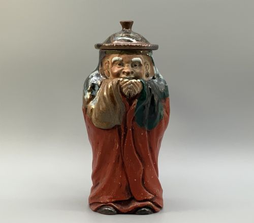 fig 5. An antique Japanese Sumida Gawa lidded pottery jug sculpted in the form of a robed figure with red attire, green glaze drips, and a matching fitted lid.