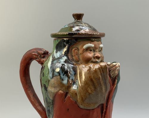 fig 9. An antique Japanese Sumida Gawa lidded pottery jug sculpted in the form of a robed figure with red attire, green glaze drips, and a matching fitted lid.