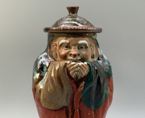 fig 10. An antique Japanese Sumida Gawa lidded pottery jug sculpted in the form of a robed figure with red attire, green glaze drips, and a matching fitted lid.