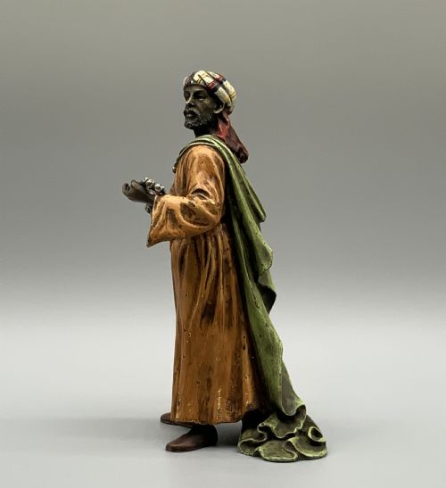 fig 3. A cold-painted bronze Orientalist figure wearing a turban and ochre robe, standing next to a small table displaying wares.