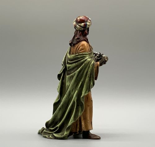 fig 5. A cold-painted bronze Orientalist figure wearing a turban and ochre robe, standing next to a small table displaying wares.
