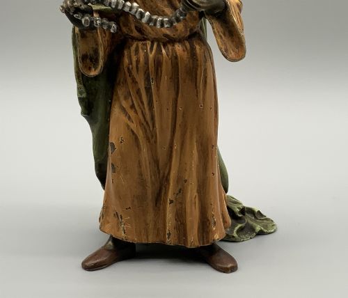 fig 9. A cold-painted bronze Orientalist figure wearing a turban and ochre robe, standing next to a small table displaying wares.