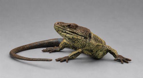fig 1. An antique cold-painted bronze sculpture depicting a realistic lizard with textured yellow and brown skin, blue accents, and a long curved tail.