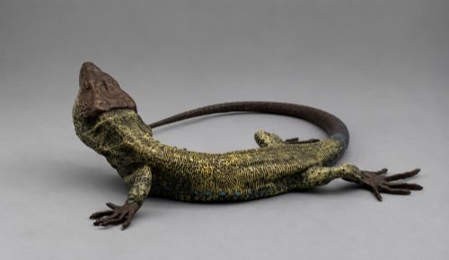 fig 3. An antique cold-painted bronze sculpture depicting a realistic lizard with textured yellow and brown skin, blue accents, and a long curved tail.