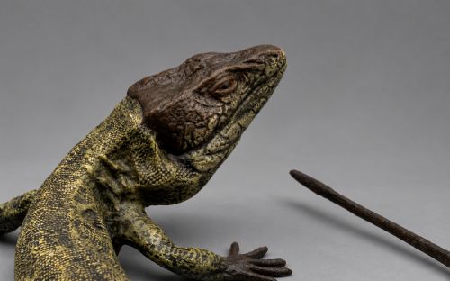 fig 5. An antique cold-painted bronze sculpture depicting a realistic lizard with textured yellow and brown skin, blue accents, and a long curved tail.