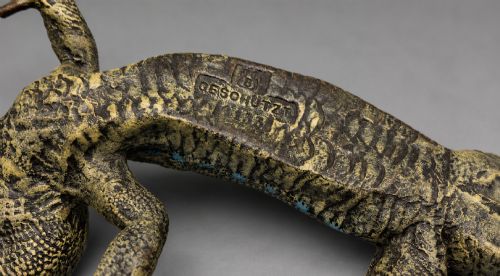 fig 9. An antique cold-painted bronze sculpture depicting a realistic lizard with textured yellow and brown skin, blue accents, and a long curved tail.