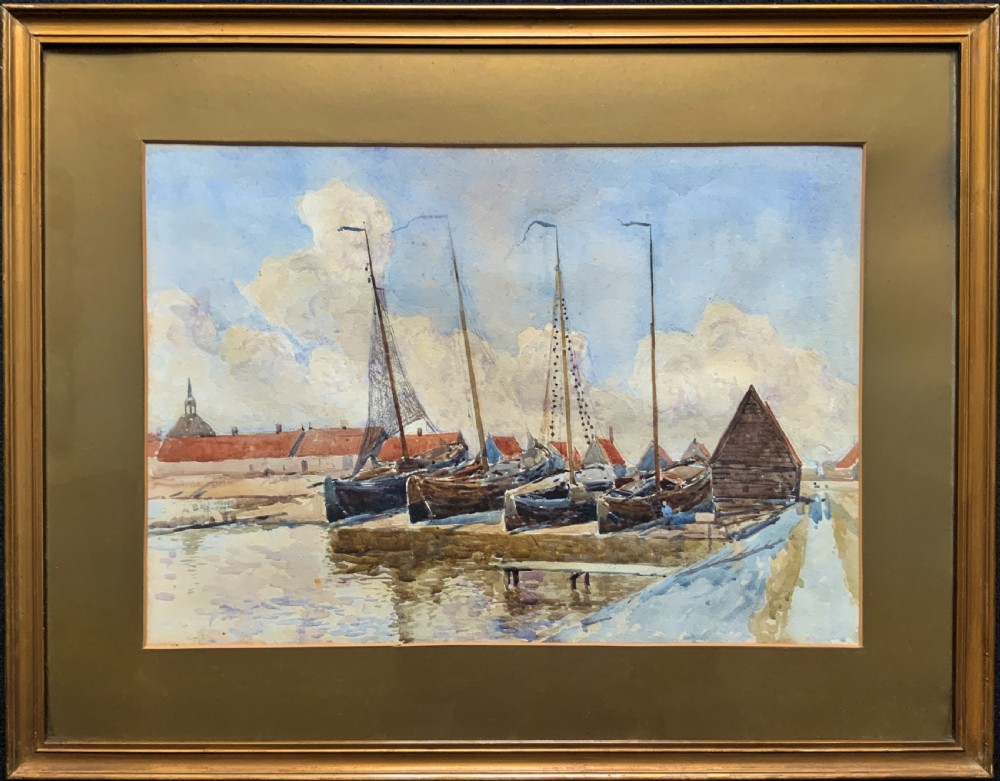 A 19th-century watercolour painting depicting several wooden sailing boats docked at a boat yard alongside buildings, housed within a wide gilt mount and thin gilt frame.