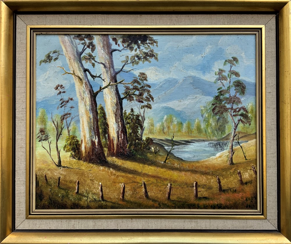 A mid-century oil landscape painting depicting tall gum trees beside a lake against blue mountains, framed in a gilt and fabric-lined wooden frame.