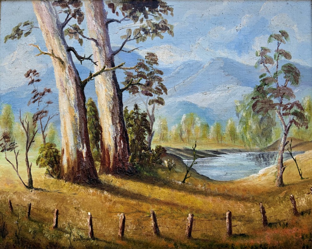 A mid-century oil landscape painting depicting tall gum trees beside a lake against blue mountains, framed in a gilt and fabric-lined wooden frame. View II