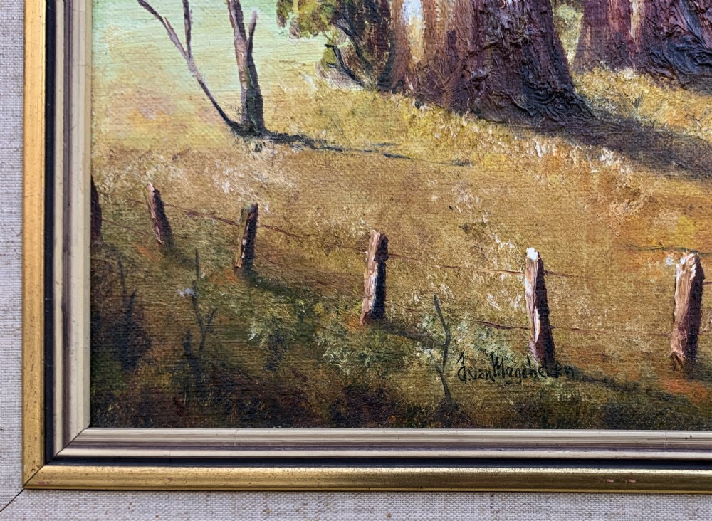 A mid-century oil landscape painting depicting tall gum trees beside a lake against blue mountains, framed in a gilt and fabric-lined wooden frame. View VIII