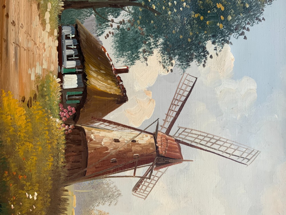 A horizontal oil painting depicting a rural Dutch scene with a tall windmill, thatched cottages, and a calm pond, framed in an ornate gilded frame. View X