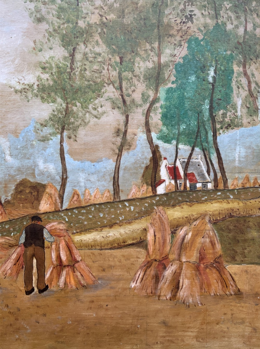 A mid-20th-century naive oil painting depicting agricultural workers gathering hay bales in a field beside a timber windmill, thatched cottages, and trees, presented in a gilt frame. View VI