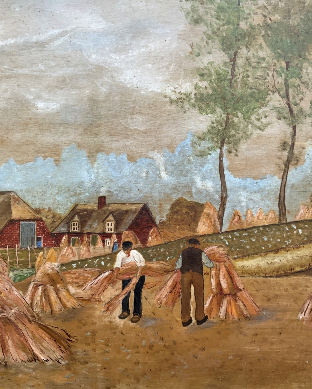 A mid-20th-century naive oil painting depicting agricultural workers gathering hay bales in a field beside a timber windmill, thatched cottages, and trees, presented in a gilt frame. View VII