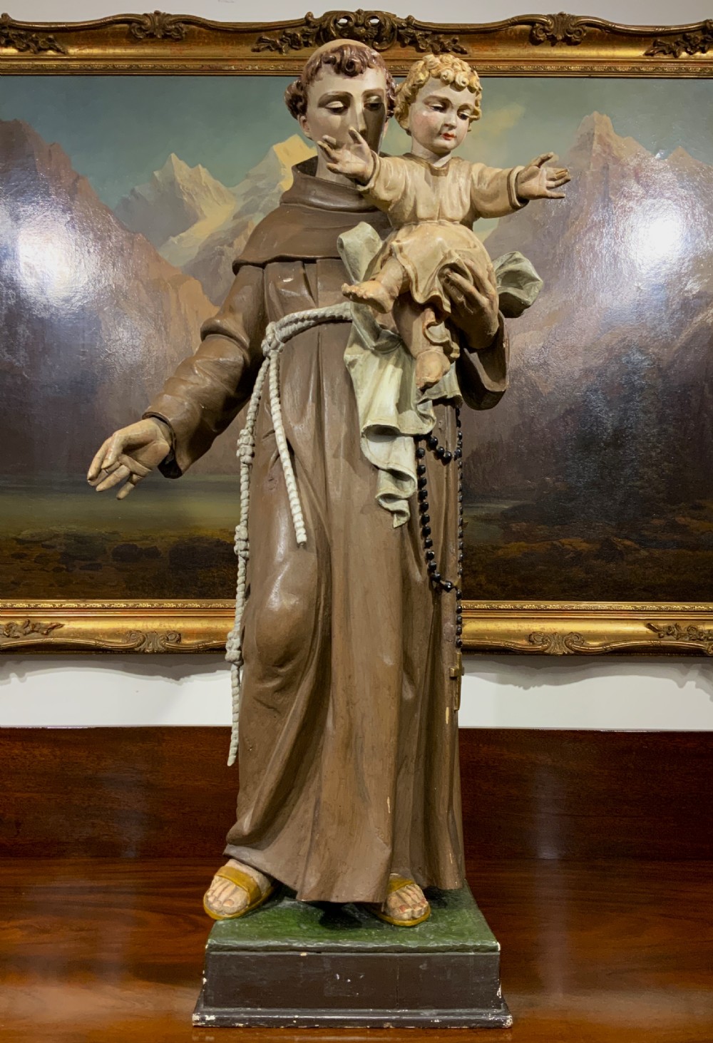 A carved polychrome wood statue depicting a saint in a brown robe holding the infant Jesus.