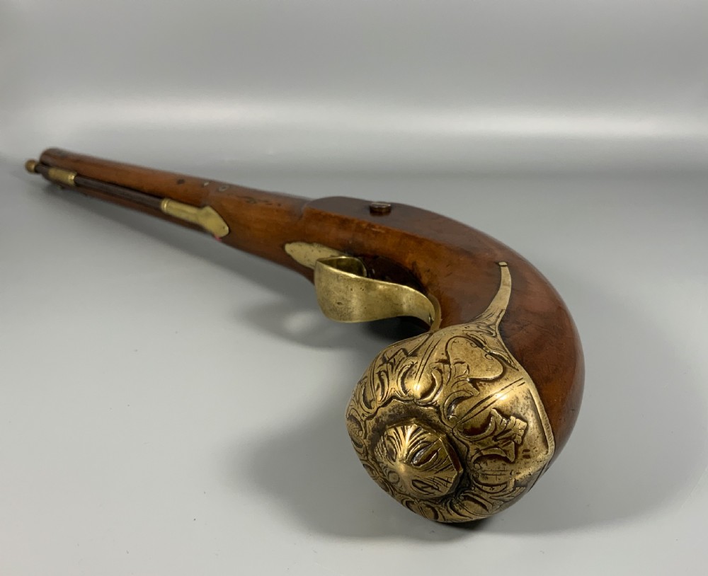 A 19th-century Regency smooth-bore percussion pistol with a carved walnut stock, engraved steel lockwork, and brass fittings. View V