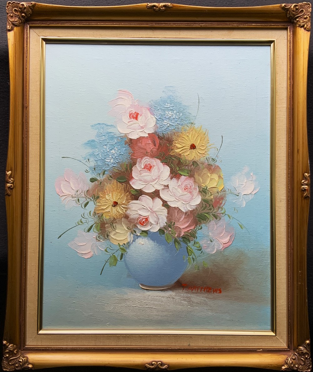 A framed post-war floral still life oil painting depicting pink, yellow, and blue flowers in a rounded blue vase within a gilt wooden frame.